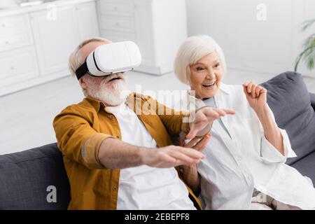 Senior man using vr headset near smiling wife in living room Stock Photo