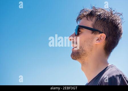 Portrait of man with sunglasses. Profile of male with glasses of sun. Confident handsome guy in sunglasses on blue sky background. Stylish man in blac Stock Photo