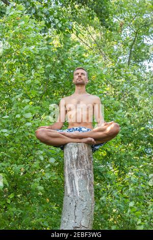 Man sitting on long tree trunk and meditating on foliage background. Young man sitting in lotus pose on tree stem. Guy man feeling free in nature. Pea Stock Photo