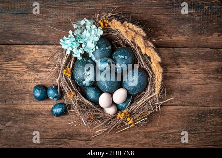 The nest is decorated with blue flowers with Easter marble-blue eggs on a wooden background. Stock Photo