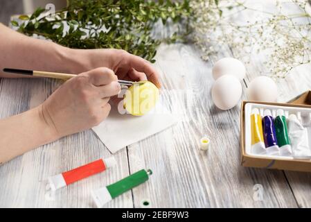 Female hands painting an egg in yellow with a brush on a wooden table. Preparing for Easter Stock Photo