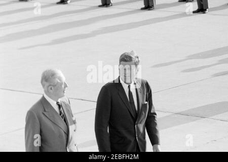Arrival ceremonies for Harold Macmillan, Prime Minister of Great Britain, 4:50PM. President John F. Kennedy walks with Prime Minister of Great Britain, Harold Macmillan (left), during arrival ceremonies in honor of Prime Minister Macmillan. Andrews Air Force Base, Maryland. [White spots in center and scratch along bottom of image are original to the negative.]
