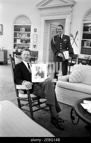 Visit of Judy Garland, Danny Kaye, Carol Burnett and Richard Adler, 12:30PM. Entertainer, Danny Kaye (holding a portrait of President John F. Kennedy), sits in President Kennedyu0027s rocking chair. Military Aide to the President, General Chester V. Clifton, stands at right. Oval Office, White House, Washington, D.C. Stock Photo