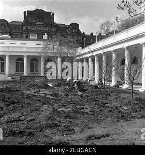 Rose Garden, construction progress photographs. Three unidentified workers dig into a section of the lawn at the Rose Garden construction site; an unidentified person (back right, partially hidden) looks on from the West Wing Colonnade. The Executive Office Building is visible in the background. White House, Washington, D.C. Stock Photo