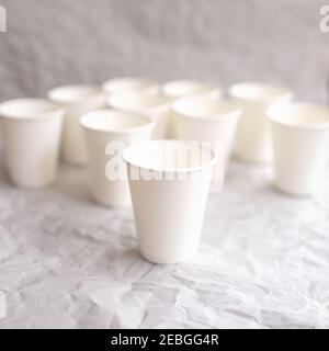 disposable cups made of white paper are laid out on gray crumpled paper in a geometric pattern Stock Photo