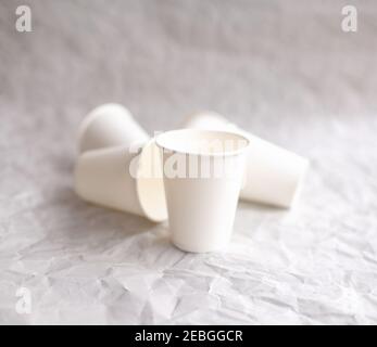 disposable cups made of white paper are laid out on gray crumpled paper in a geometric pattern Stock Photo