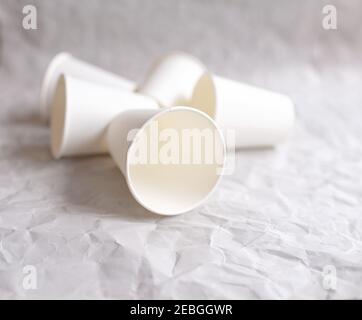 disposable cups made of white paper are laid out on gray crumpled paper in a geometric pattern Stock Photo