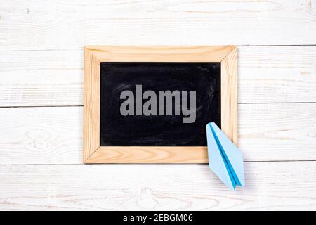 Black board with paper plane on white wooden background. Back to school and education concept. Stock Photo