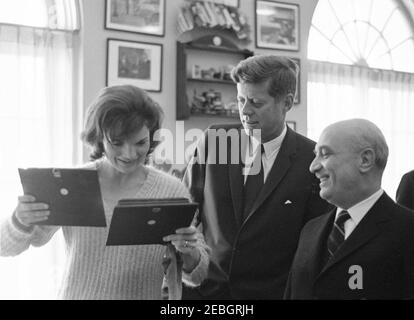 Meeting with the Prime Minister of Italy Amintore Fanfani, 10:00AM. First Lady Jacqueline Kennedy looks at two framed bas relief sculptures presented by Prime Minister of Italy, Amintore Fanfani (right); President John F. Kennedy stands in center. Office of Evelyn Lincoln (Presidentu2019s Personal Secretary), White House, Washington, D.C. Stock Photo