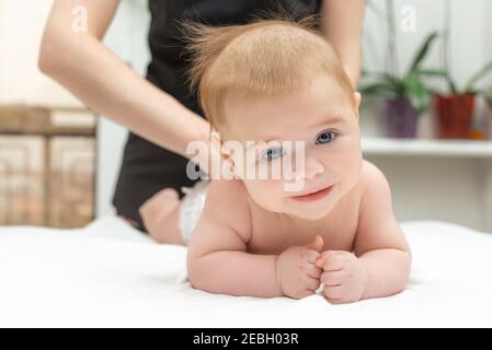 Portrait of a three-month-old baby boy. Newborn baby lies on his stomach and looks at the camera with interest while mom doing massage. A surprised ba Stock Photo