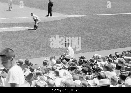 1962 All Star Baseball Game at D.C. Stadium, 12:52PM. President John F. Kennedy (partially hidden in crowd, wearing sunglasses) and others watch the 32nd Major League Baseball (MLB) All-Star Game at D.C. Stadium, Washington, D.C. Vice President Lyndon B. Johnson stands in center, right of President Kennedy; first base coach for the National League, Casey Stengel (manager of the New York Mets), stands on the field in background. Stock Photo