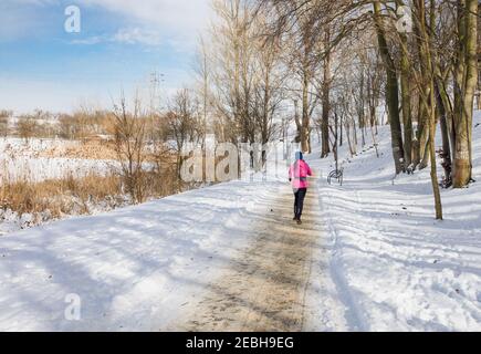 A runner on a snowy path around a frozen lake, a winter workout in the park. Stock Photo
