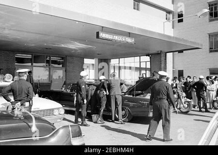 Trip to Texas: Parkland Hospital (exterior); Presidentu2019s limousine; Love Field, Presidentu2019s body borne onto Air Force One. Police officers gather around the Presidential limousine (Lincoln-Mercury Continental) in front of an entrance to Parkland Hospital in Dallas, Texas, following the arrival of President John F. Kennedy. Stock Photo