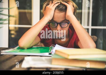 Tired student doing homework at home sitting outdoor with school books and newspaper. Boy weary due to heavy study. Kid asleep on the copybook after l Stock Photo