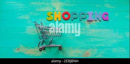 Empty shopping cart and inscription SHOPPING on green wood background. Word shopping and trolley from one side. Concept of online shopping. Web banner Stock Photo