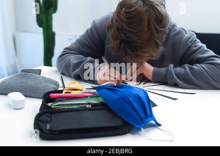 Teen drawing alone at home during covid-19 lockdown. Caucasian young boy doing homeworks. Student learning in pandemic days Child study at home school Stock Photo