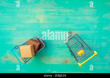 Shopping cart filled with boxes and another one empty on wooden background. Two small trolleys - empty and with boxes. Top view, copy space. Stock Photo
