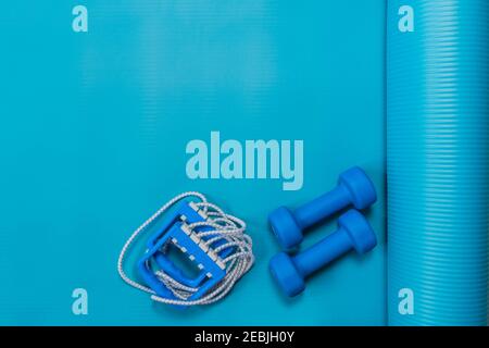 Two dumbbells, chesty expander on exercise yoga mat at home or in fitness studio. Blue color tools for training, sport, and activity. Fitness healthy Stock Photo