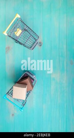 Shopping cart empty and another one filled with boxes on vintage blue wooden background. Two small trolleys - empty and with boxes. Top view, copy spa Stock Photo