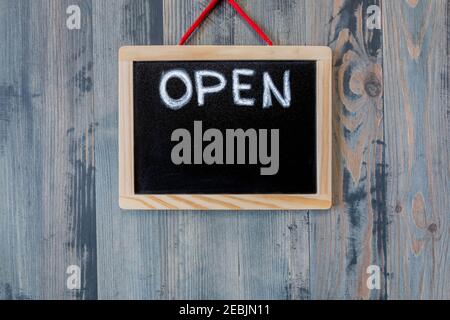 Board with lettering OPEN hangs on wood background. Board with sign OPEN showing quarantine mitigation. Open sign on blackboard hanging on vintage woo Stock Photo