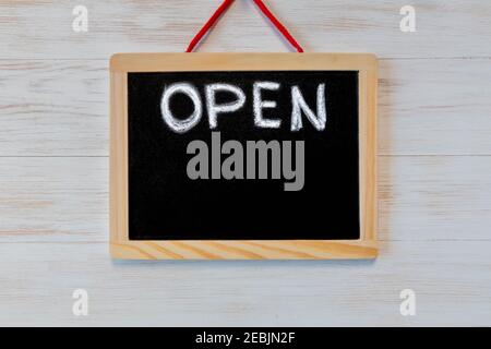 Board with sign OPEN showing quarantine mitigation. Open sign on wood background. Board with lettering OPEN hangs on blackboard hanging on vintage woo Stock Photo