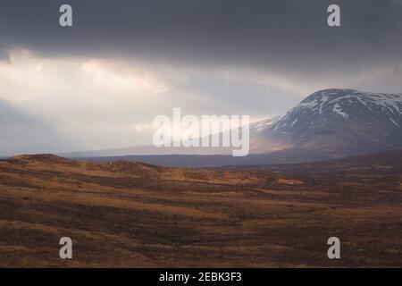 Dramatic sunlight breaks through low cloud to light up the snowcapped mountain landscape at Glencoe in the Scottish Highlands. Stock Photo