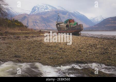 Corpach shipwreck, an abandoned vintage fishing boat, near Fort William in the Scottish Highlands with Ben Nevis mountain in the background. Stock Photo