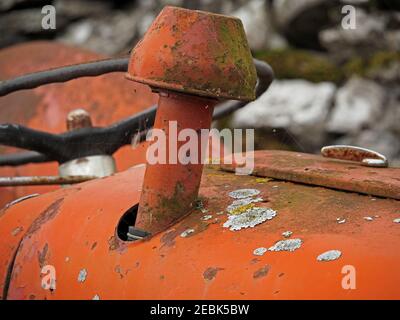 white & yellow lichen growing on faded rusted orange red paint of abandoned ancient tractor on a farm in Cumbria, England, UK Stock Photo