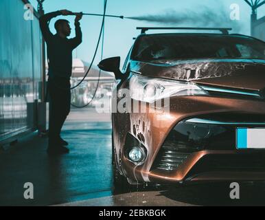 Man washing car in self serve car wash. Cleaning car using high pressure water Stock Photo