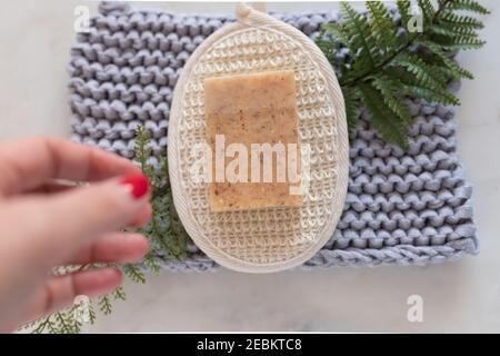 Woman hand approaching a bar of soap on a horsehair glove over a white marble board. Stock Photo