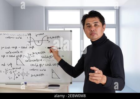 Mature professor teaching mathematics to students in classroom. Teacher man solving math problem while writing on white board with video conference. C Stock Photo