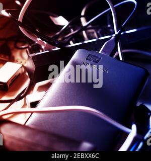 Western Digital external hard drive with the WD logo for connection to the computer, lies under blue lighting in a tangle of cables on a desk in Gifho Stock Photo