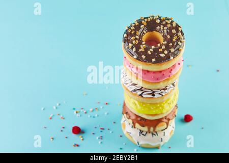 Multicolored donuts with icing and sprinkling stacked in a stack on a blue background. Stock Photo