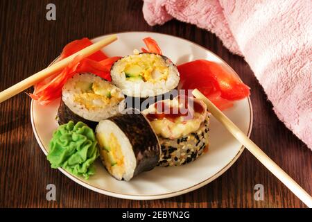 A dish of Japanese cuisine. Ready-made rolls on a white plate with wasabi sauce and pickled ginger. Stock Photo