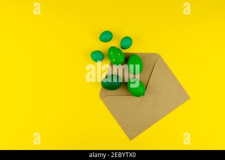 Spring Easter layout with green feathers and eggs, craft envelope on yellow background. Copy space for text for text Stock Photo