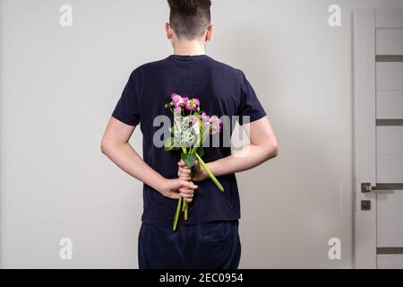 a man stands in front of the door holding a faded bouquet of flowers behind his back. separation concept Stock Photo