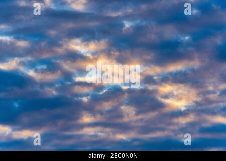 Beautiful clouds in blue sky, illuminated by rays of sun at sunset to change summer weather. Soft focus motion blur multicolored cloudscape background Stock Photo