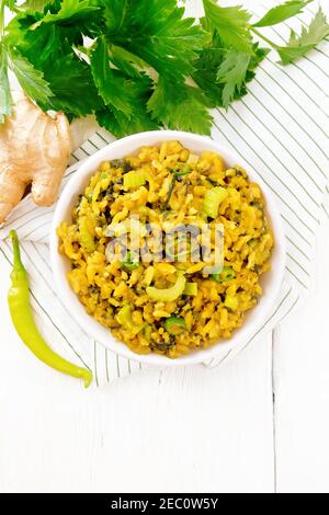 Indian national dish kichari made from mung bean, rice, stalk celery, spinach, hot pepper and spices in a bowl on a napkin, ginger on light wooden boa Stock Photo
