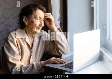 Happy senior woman sitting with her granddaughter looking at laptop making video call. Mature lady talking to webcam, doing online chat at home during Stock Photo