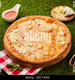 Delicious italian pizza quattro formaggi with the four cheeses Mozarella, Gorgonzola, Parmesan and Gouda on green grass background Stock Photo