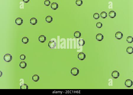 An abstract portrait of multiple round air bubbles hanging on a glass container full of water with a green background. The bubbles are perfect circles Stock Photo