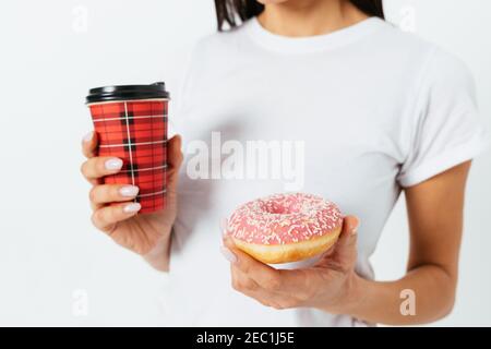 Donut and paper cup coffee in female hands on white background studio, close-up. Stock Photo