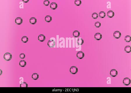 An abstract portrait of multiple round air bubbles hanging on a glass container full of water with a pink background. The bubbles are perfect circles. Stock Photo