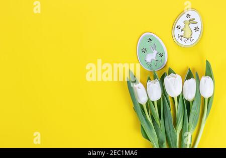 Easer postcard. White tulips and wooden bunny eggs on yellow background Stock Photo