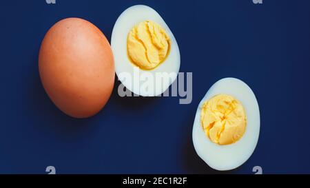 Top view of two boiled eggs, one egg still in the shell, and the other egg peeled and cut into two halves. Healthy breakfast. Stock Photo