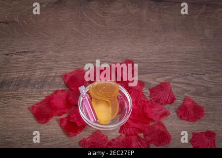 Perfumed rose water and rose flower made of soap in glassware on wooden table with rose petals. Background for copy space. Stock Photo