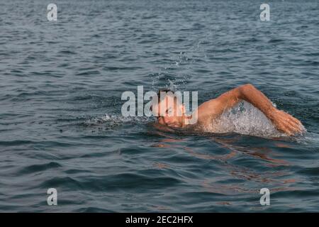 Young man is swimming fast in water on sunny and warm day Stock Photo