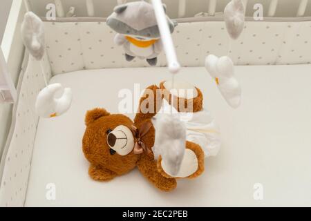 Pcture of a brown teddy bear with diaper on sitting in baby bed Stock Photo