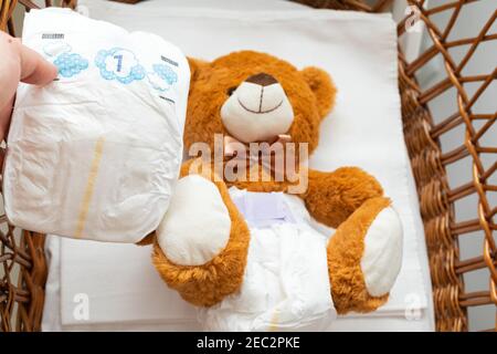 Pcture of a brown teddy bear with diaper on sitting in baby bed Stock Photo