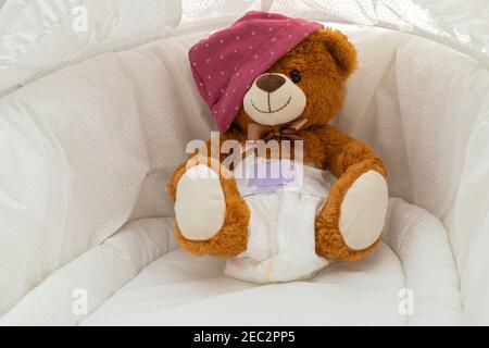 Pcture of a brown teddy bear with diaper on sitting in baby bed Stock Photo